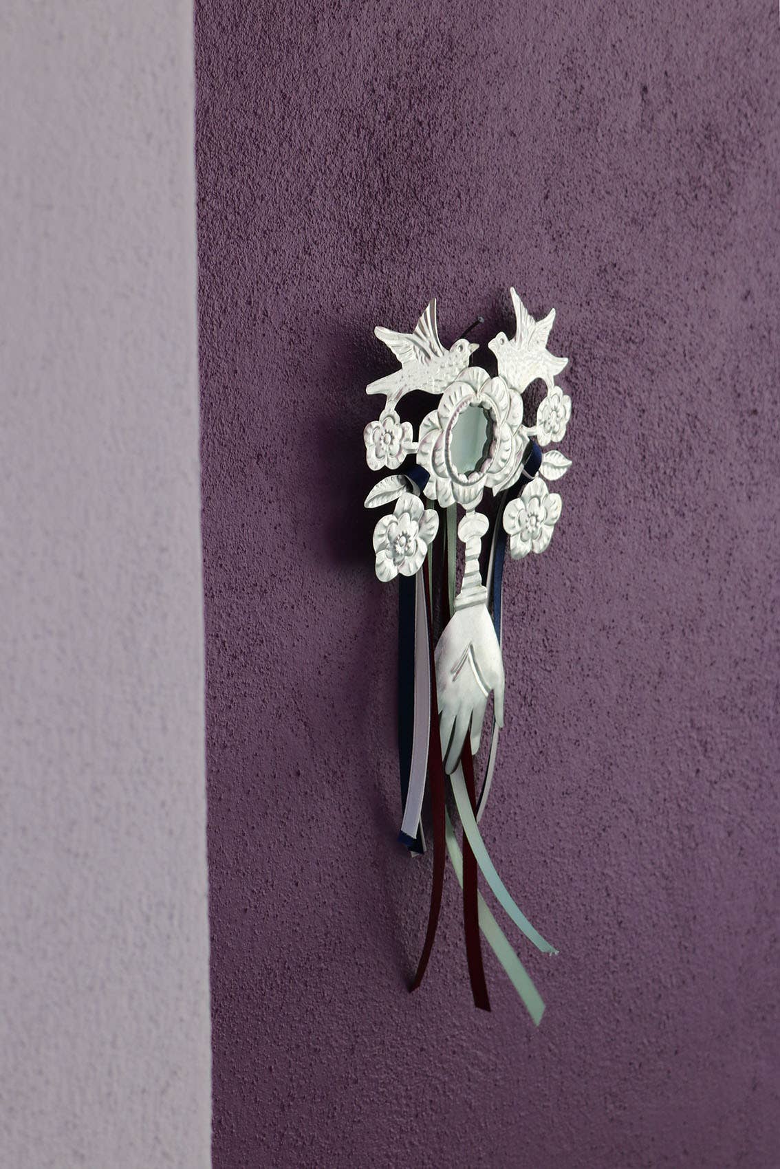 Decorative mirror made of tin with floral design and multicolored ribbons on a textured purple background