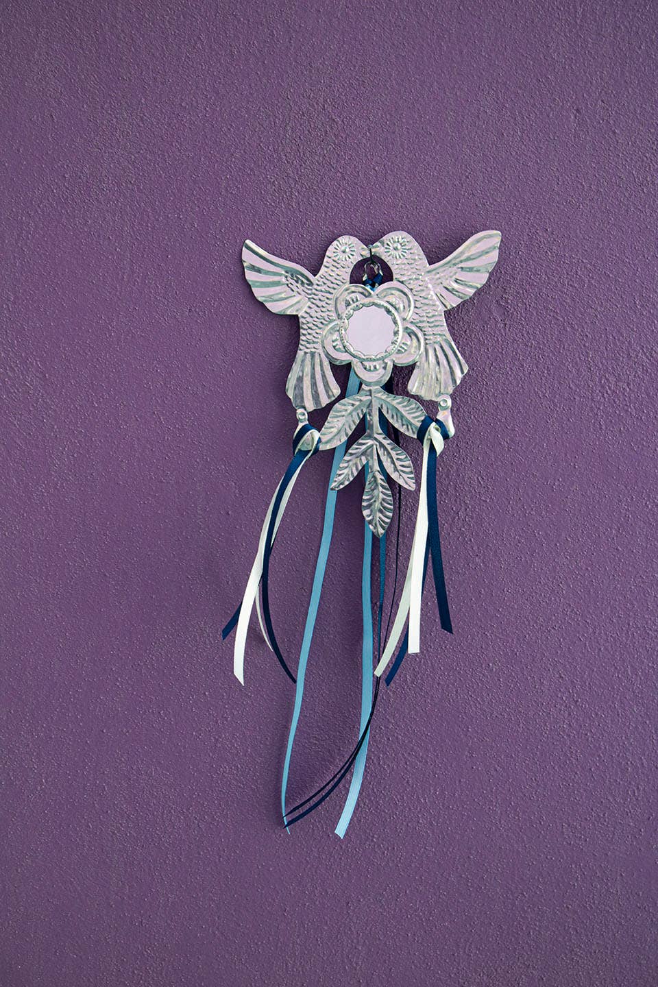 Decorative wall hanging with bird and flower design and ribbons on a purple background