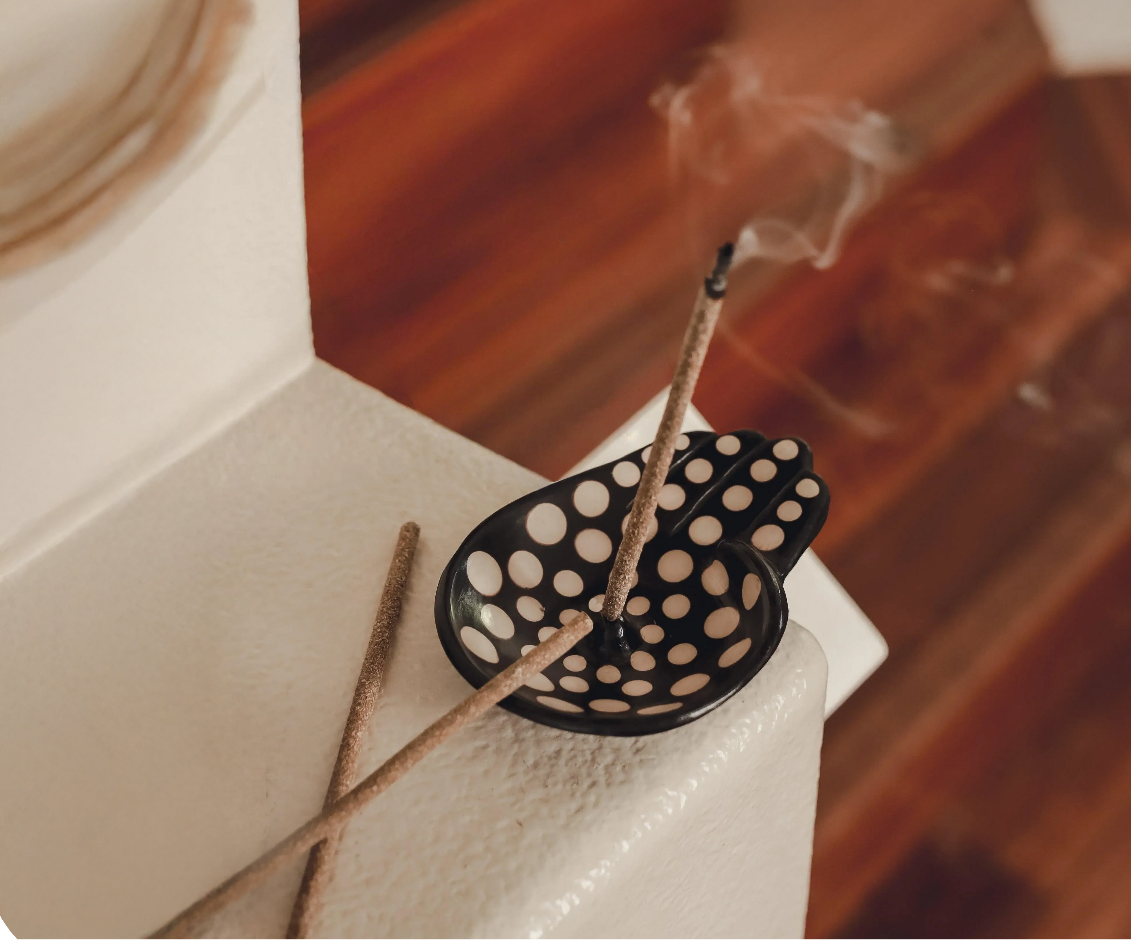 Incense sticks in a black holder with white dots on a white surface.